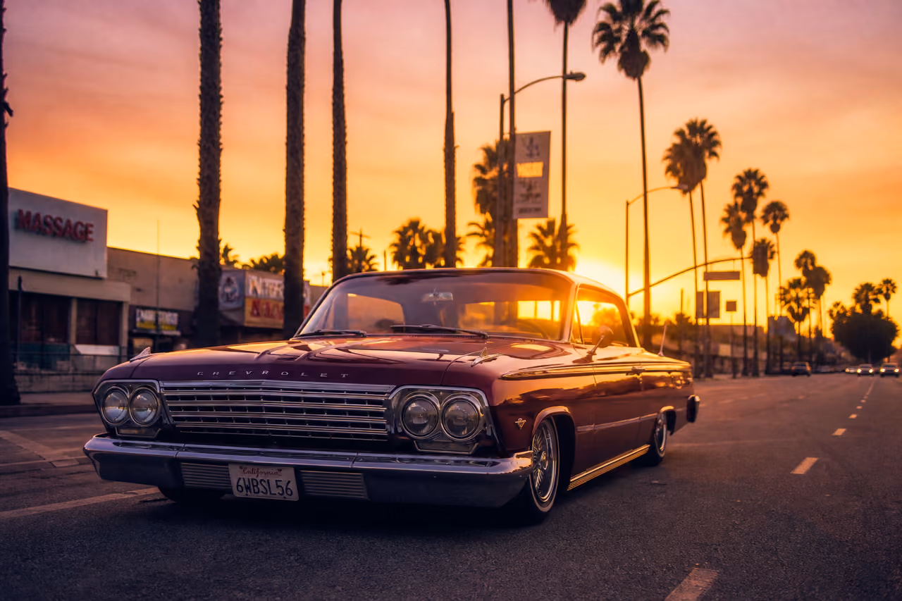 Classic Vintage Lowrider Cruising Down a Sunlit Palm Boulevard at Sunset